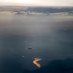 Aerial view of mountain lake against sky during sunset from plane's window