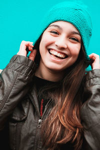 Close-up portrait of cheerful young woman wearing knit hat against turquoise background