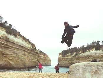 Man jumping on rock by sea against clear sky