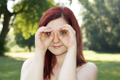 Portrait of young woman peering through hands in park