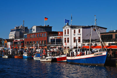 Boats moored at harbor against clear blue sky