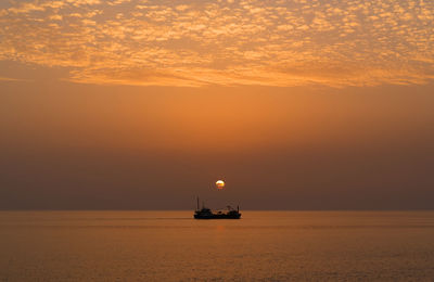 Scenic view of sea against orange sky with a boat