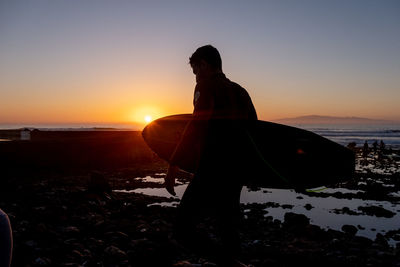 Silhouette man on beach against sky during sunset