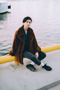 Full length of young woman sitting against lake