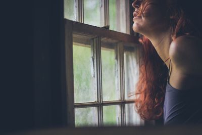 Side view of woman looking through window