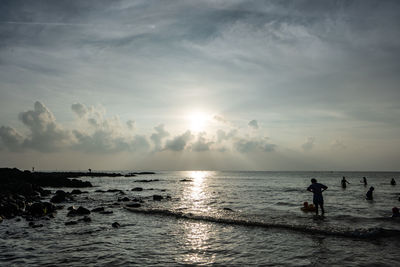 Silhouette people on beach against sky during sunset