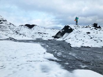 Low angle view of man standing on snowcapped mountain against sky