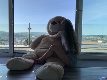 Young woman hugging bear sitting by window