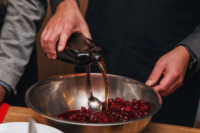 Hands of a man pouring alcohol into cherries. process of preparing dessert.