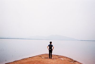 Rear view of man standing at lakeshore against clear sky