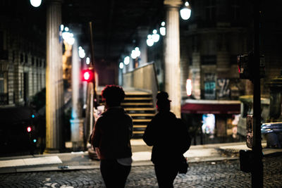 Rear view of woman walking on illuminated street at night