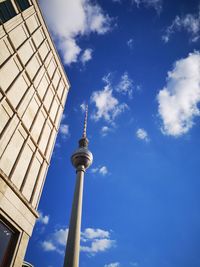 Low angle view of communications tower against blue sky during sunny day in city