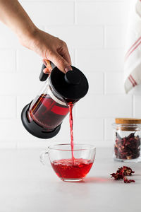 Tea from hibiscus petals is poured from a teapot into a transparent cup.