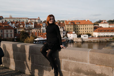 Full length portrait of young woman standing against buildings in city