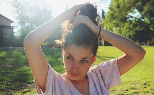 Young woman tying hair on grassy field during sunny day