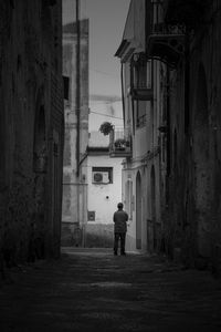 Rear view of man walking on road along buildings