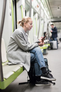 Side view of woman using mobile phone sitting at subway train