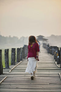 Woman walking on wooden walkway against sky