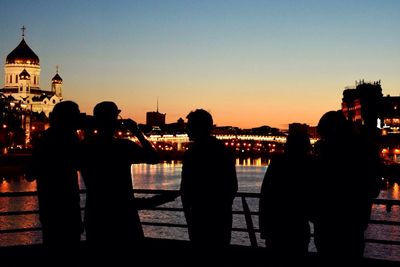 Silhouette people standing in front of river against sky during sunset