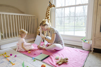 Young mom reading to her toddler daughter in her room