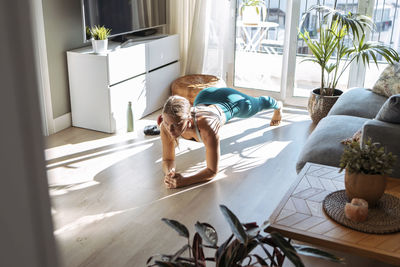 Woman practicing plank position while exercising on floor at home