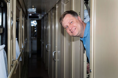 A smiling, happy adult man looks out from his compartment in the train car.