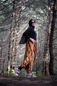 Woman standing by tree trunk in forest