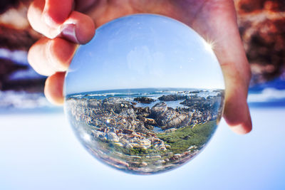 Close-up of hand holding crystal ball against sea and sky