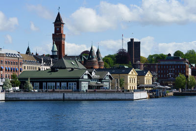 Buildings at waterfront against cloudy sky