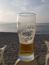 Close-up of beer glass on beach against sky