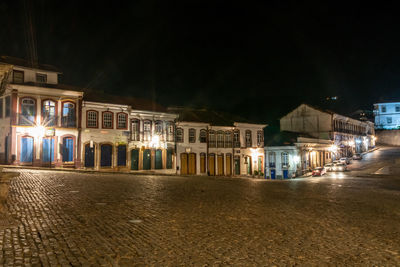 Illuminated buildings by street against sky at night