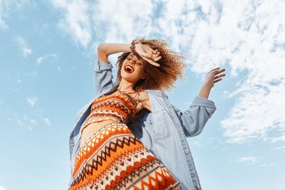 Low angle view of young woman standing against sky