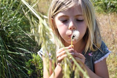 Close-up of girl blowing dandelion on field