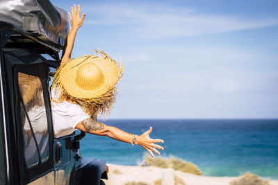 Rear view of excited woman looking at blue sea while sitting in car during sunny day