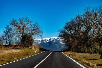 Road amidst trees against clear blue sky