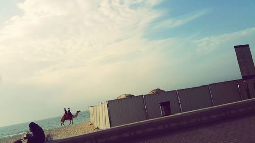 Man riding woman walking on road against sky