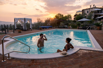 People on swimming pool against sky during sunset