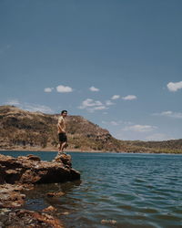 Man standing on rock by sea against sky