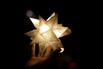 Close-up of hand holding illuminated lighting equipment against black background