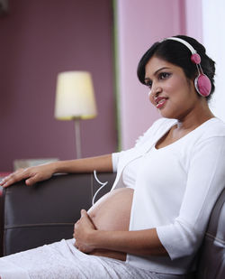 Pregnant woman listening music while sitting on sofa at home