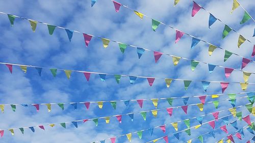 Low angle view of flags hanging against cloudy blue sky