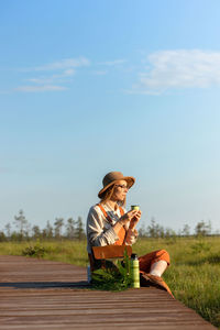 Naturalist woman resting on boardwalk, drinking tea, enjoying the moment at sunset. ecotourism