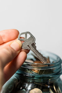 Close-up of hand holding key against white background, coin jar