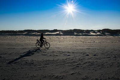 Man riding bicycle on beach against clear sky