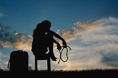 Silhouette young woman sitting on table against sky during sunset