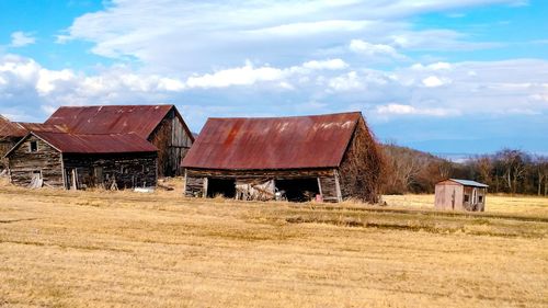 Abandoned farm buildings in field against sky