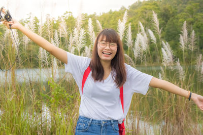 Portrait of woman with arms outstretched standing against plants