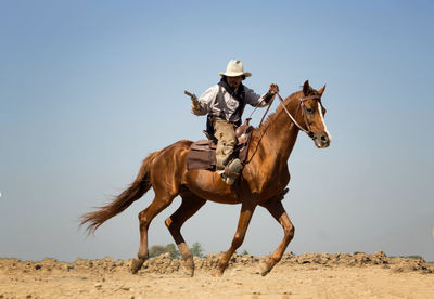 Man with gun riding horse against sky