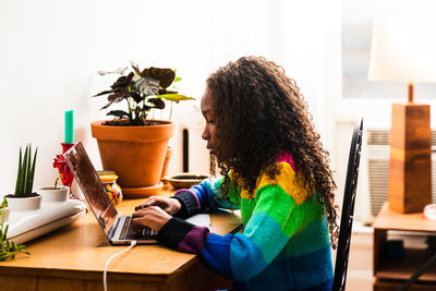 Side view of girl using laptop while sitting at table in living room