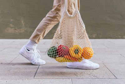 Side view of cropped unrecognizable male standing with eco friendly mesh bag full of fresh fruits in city street